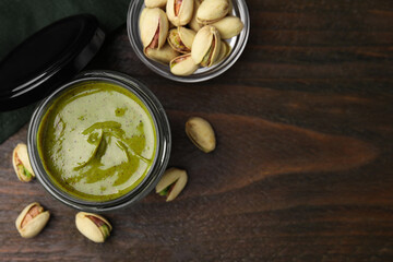 Tasty pistachio cream in jar and nuts on wooden table, flat lay. Space for text