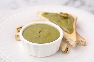Tasty pistachio cream in bowl and toasts on plate, closeup