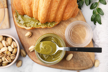 Tasty pistachio cream in jar, spoon and croissant on light table, flat lay