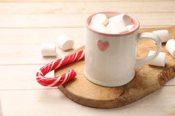 Tasty hot chocolate with marshmallows and candy cane on light wooden table, closeup