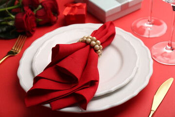 Place setting with gift boxes and bouquet of roses on red table, closeup. Romantic dinner