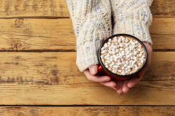 Woman with cup of tasty hot chocolate and marshmallows at wooden table, top view. Space for text
