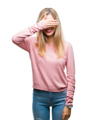 Young beautiful blonde woman wearing pink winter sweater over isolated background smiling and laughing with hand on face covering eyes for surprise. Blind concept.