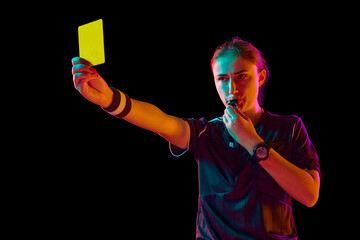 Disciplinary action. Female referee showing yellow card against black studio background in neon...