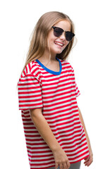 Naklejka premium Young beautiful girl wearing sunglasses over isolated background looking away to side with smile on face, natural expression. Laughing confident.