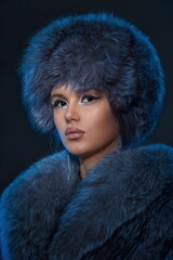 Portrait of a young girl with exquisite makeup wearing a blue fur coat and hat