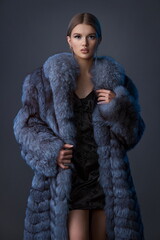 A young girl with exquisite makeup in a blue fur coat and a short black dress.