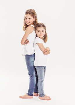 Studioportrait von zwei Schwestern R&uuml;cken am R&uuml;cken, barfuss in Jeans. L&auml;cheln in die Kamera