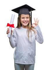 Young beautiful girl wearing graduate cap holding degree over isolated background doing ok sign...