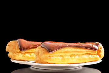 Two delicious chocolate eclairs on a ceramic saucer, close-up isolated on a black background.