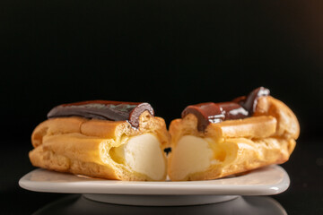 Two halves of a delicious chocolate eclair on a white ceramic plate, close-up isolated on a black...