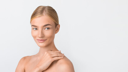 Confident blonde woman with hand on her shoulder, studio portrait