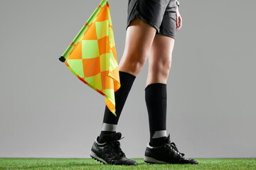 Cropped image of female legs, referee on field standing with flag to signal game rules against grey...