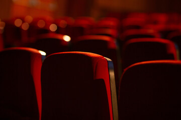 Detalhe de um teatro vazio. Várias fileiras de poltronas vermelhas fotografadas por trás....