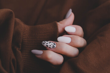 Woman's hand with a beautiful oval-shaped manicure. Autumn trend, beige color polishing with...