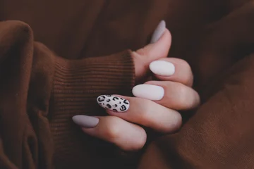Fotobehang Woman's hand with a beautiful oval-shaped manicure. Autumn trend, beige color polishing with leopard pattern on nails with gel polish, shellac. © smile35