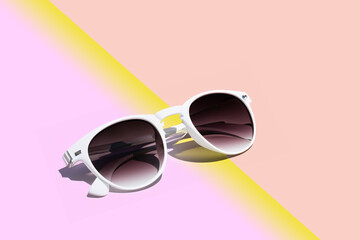 summer accessory. white women's sunglasses lie on a pink yellow gradient background close-up, creative concept