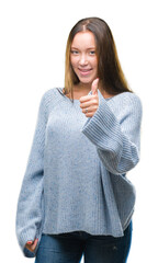 Young beautiful caucasian woman wearing winter sweater over isolated background doing happy thumbs up gesture with hand. Approving expression looking at the camera with showing success.