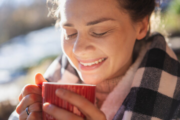 Young woman enjoying a sunny early spring morning on the terrace drinking a hot drink, close up