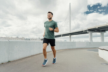 Active man jogging on a city pathway with a modern bridge in the backdrop, showcasing a blend of fitness and urban architecture.