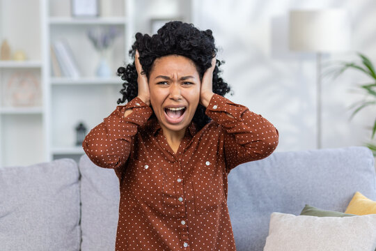 Close-up Photo Of A Worried And Angry Young African-American Woman Sitting On The Sofa At Home And Screaming Loudly With Her Hands Over Her Ears