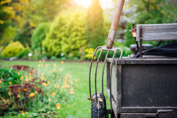 A pitchfork and an agricultural cart on the background of a blooming green garden and lawn. Gardening, seasonal work, rural life and farming business