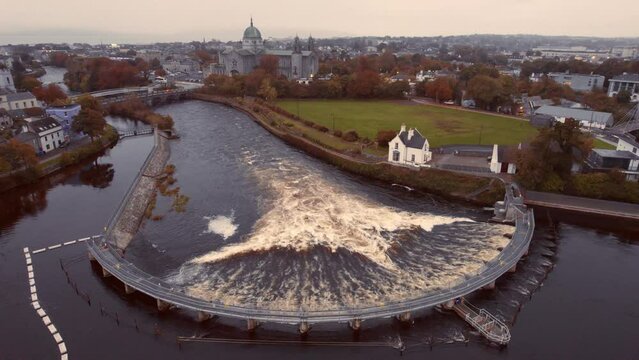 Water flows in half circle dam in Galway city, Ireland. River Corrib by Galway cathedral building. Aerial view. Town scene with landmark and bridge over a fast flowing river.