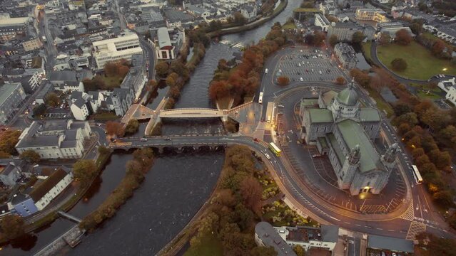 Aerial view on Galway Cathedral building and two bridges over river Corrib, pedestrian and for vehicles. Popular town landmark. Dusk time with city lights illumination and light traffic. Ireland