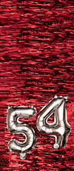 Silver foil balloon number number 54 on a background of red tinsel decoration. Birthday greeting...