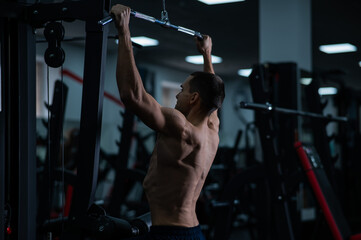 Fototapeta na wymiar A man does a chest pulldown in the gym.