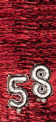 Silver foil balloon number number 58 on a background of red tinsel decoration. Birthday greeting...