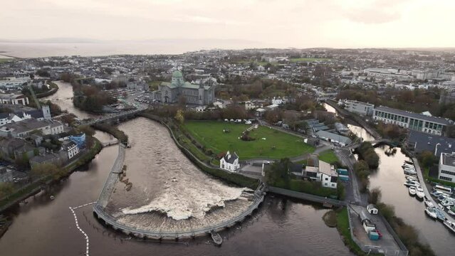 Water flows in half circle dam in Galway city, Ireland. River Corrib by Galway cathedral building. Aerial view. Town scene with landmark and bridge over a fast flowing river.