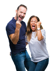 Fototapeta premium Middle age hispanic casual couple over isolated background very happy and excited doing winner gesture with arms raised, smiling and screaming for success. Celebration concept.