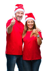 Middle age hispanic couple wearing christmas hat over isolated background doing happy thumbs up gesture with hand. Approving expression looking at the camera with showing success.