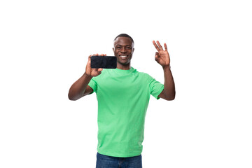 young charismatic american man in green t-shirt and jeans showing smartphone screen with mockup