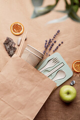 Fototapeta na wymiar Eco shopping bag with cutlery, apples, lavender on crumpled paper mock up. Sustainable lifestyle. Natural eco-friendly, zero waste tableware, blurred foreground.
