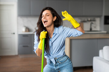 Energetic woman singing with mop in stylish kitchen