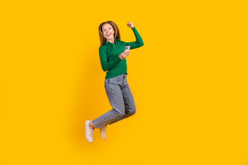Full body length size photo of overjoyed teen girl jump up finally received credit ecard in phone isolated on yellow color background