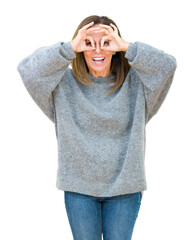 Beautiful middle age woman wearing winter sweater over isolated background doing ok gesture like binoculars sticking tongue out, eyes looking through fingers. Crazy expression.