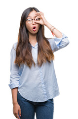 Young asian business woman wearing glasses over isolated background doing ok gesture shocked with surprised face, eye looking through fingers. Unbelieving expression.