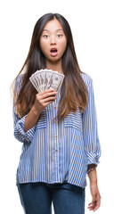 Young asian woman holding dollars over isolated background scared in shock with a surprise face, afraid and excited with fear expression