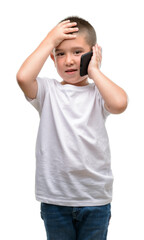 Fototapeta premium Dark haired little child using a smartphone stressed with hand on head, shocked with shame and surprise face, angry and frustrated. Fear and upset for mistake.