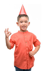 Dark haired little child wearing birthday cap doing ok sign with fingers, excellent symbol