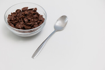 Choco cereals served in glass bowl with spoon on white background with copy space