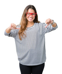 Young beautiful brunette woman wearing stripes sweater and red glasses over isolated background looking confident with smile on face, pointing oneself with fingers proud and happy.