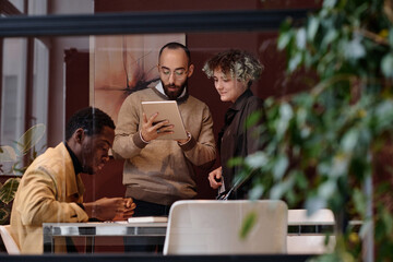 Man showing information on tablet to his female colleague, their black coworker sitting next to them