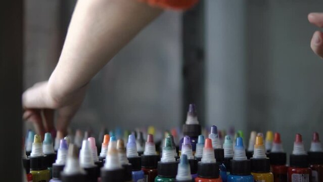 Color selection. Tubes with paints. Ink for tattoos. The girl chooses the color. All the colors of the rainbow. Bottles with colored paints. Female hand selects tubes with paint for drawing.