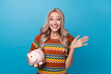 Photo of friendly sweet lady wear print shirt waving arm hi holding pig cash box isolated blue...