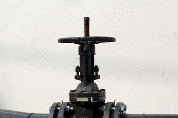 Close up of the big black valve on the pipeline with white wall background.