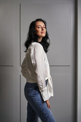 A vision of modern beauty, the brunette in a white shirt and jeans stands out against the stylish grey wall, harmonizing with the chic interior.